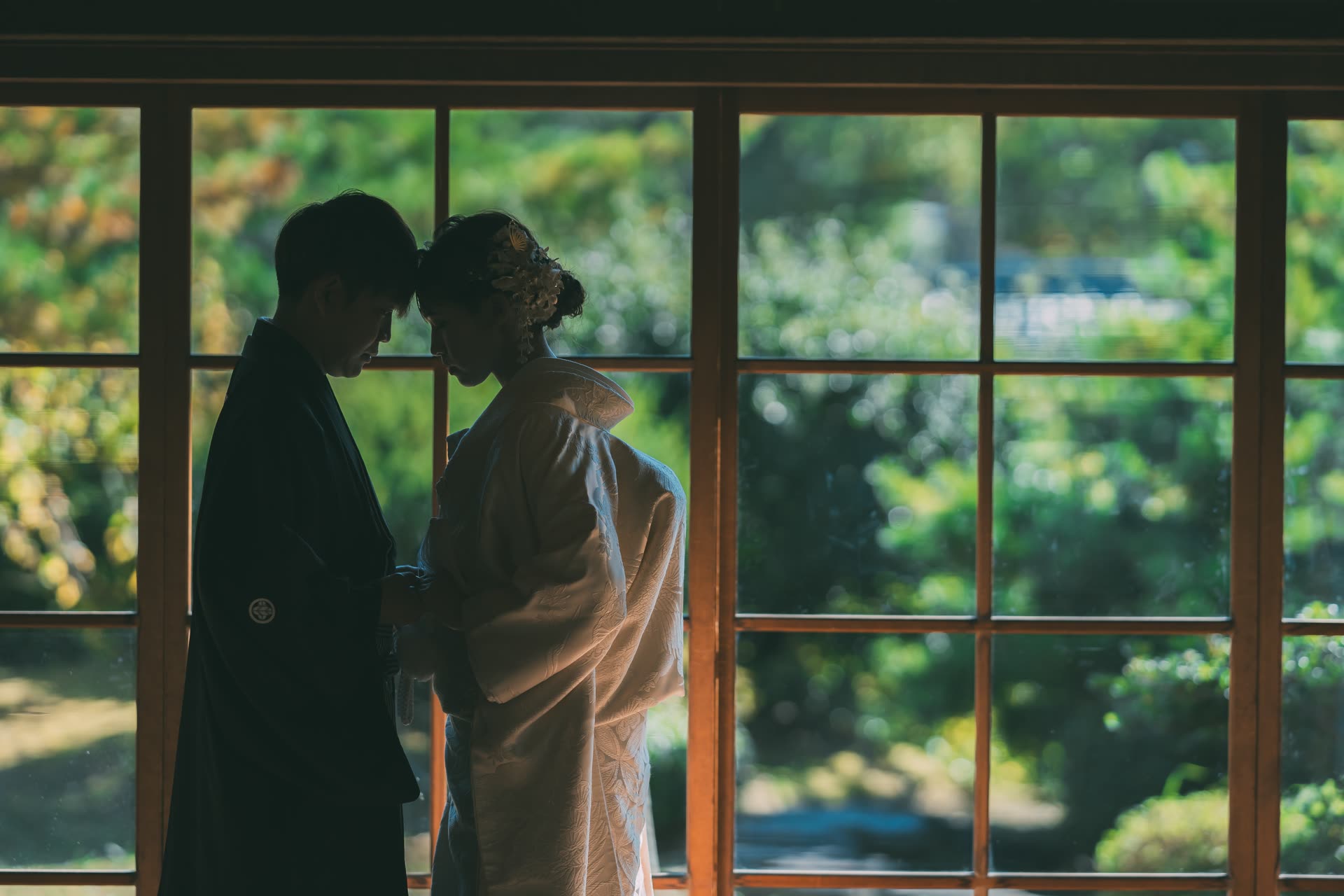 Silhouette of a couple in kimono against a garden window in a traditional Japanese house