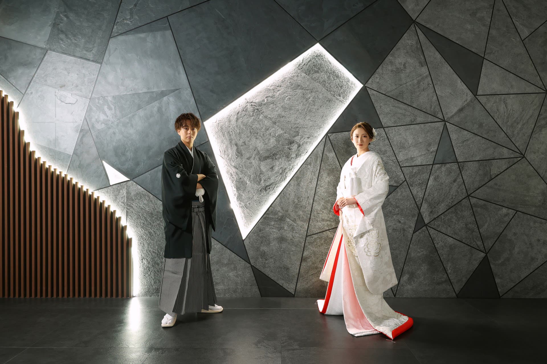 Couple in traditional Japanese wedding kimono against a sculpted geometric wall in a Tokyo studio