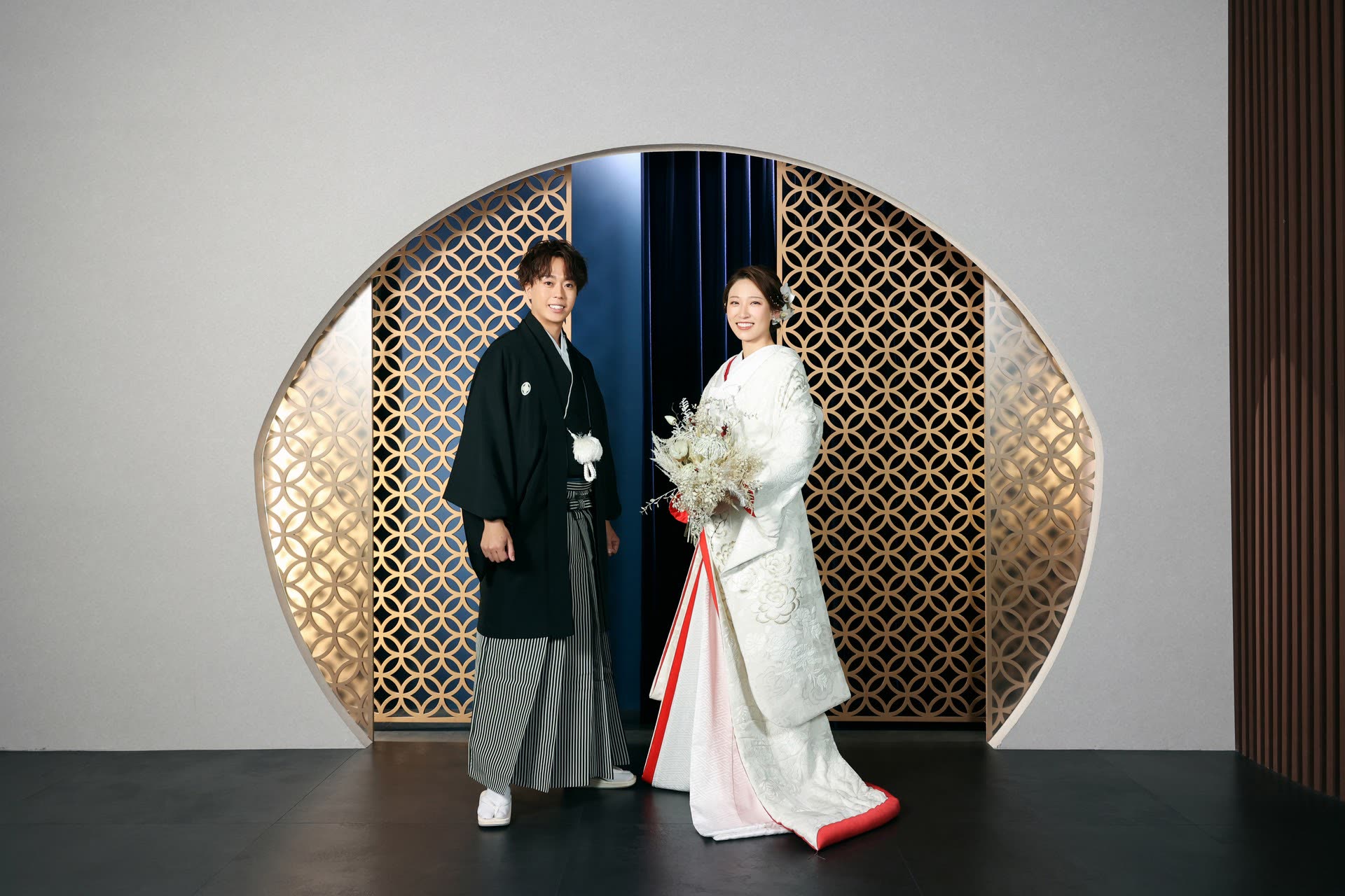Bride in shiromuku and groom in montsuki-hakama framed by a round latticed window