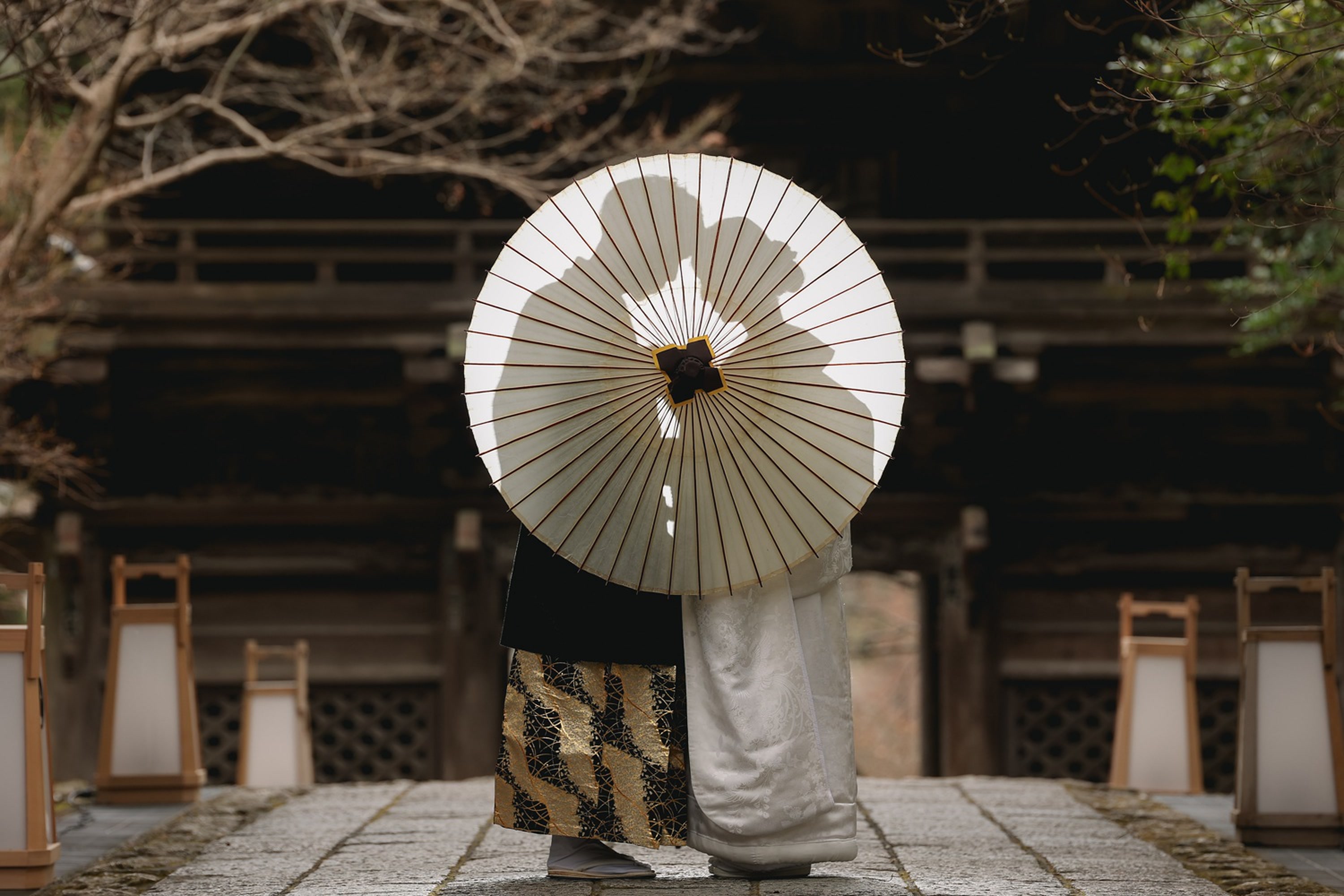 Couple in kimono behind a paper wagasa parasol at a shrine gate in Japan, on a pre-wedding photoshoot
