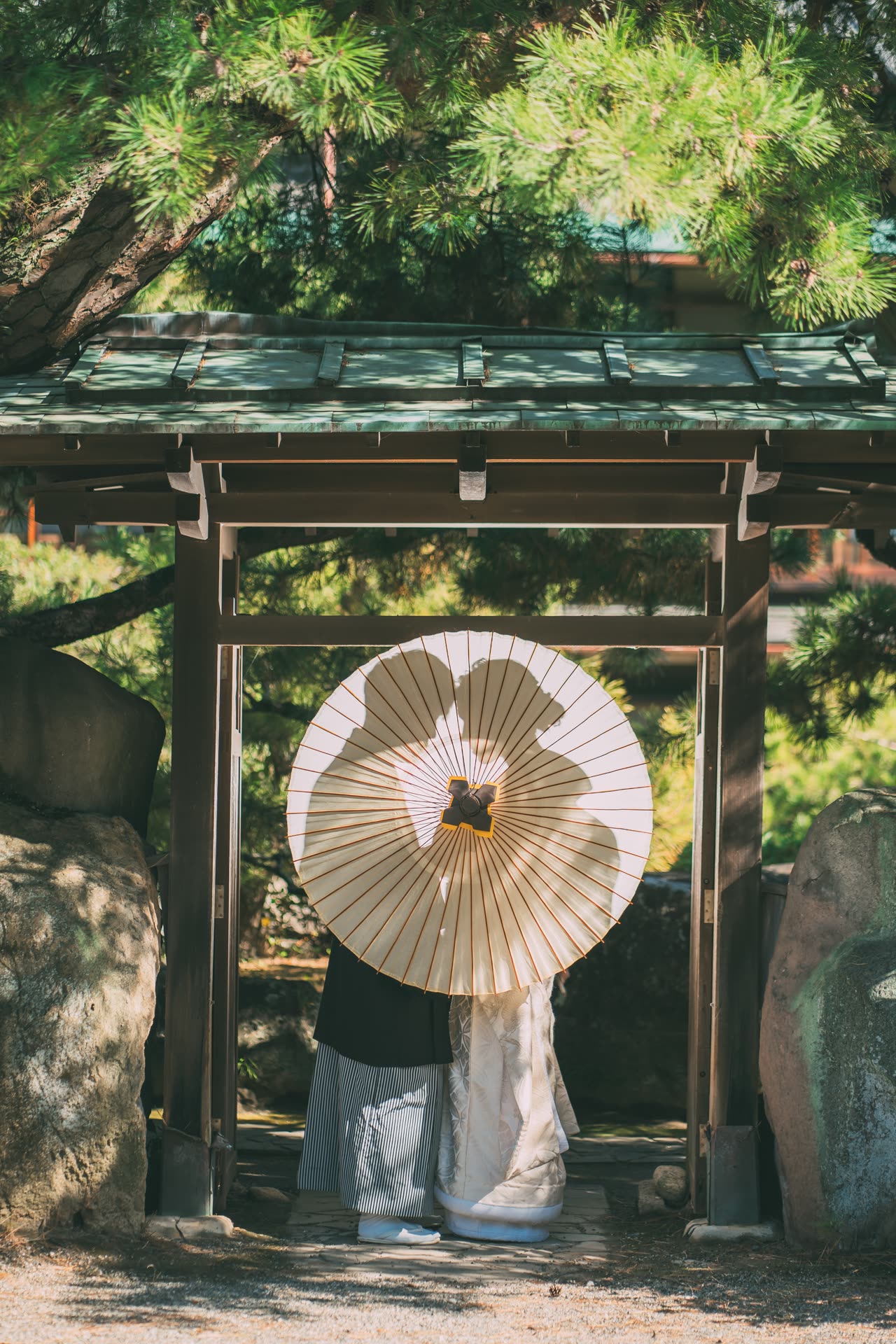 Couple hidden behind a paper wagasa parasol beneath a wooden garden gate at a Japan pre-wedding shoot