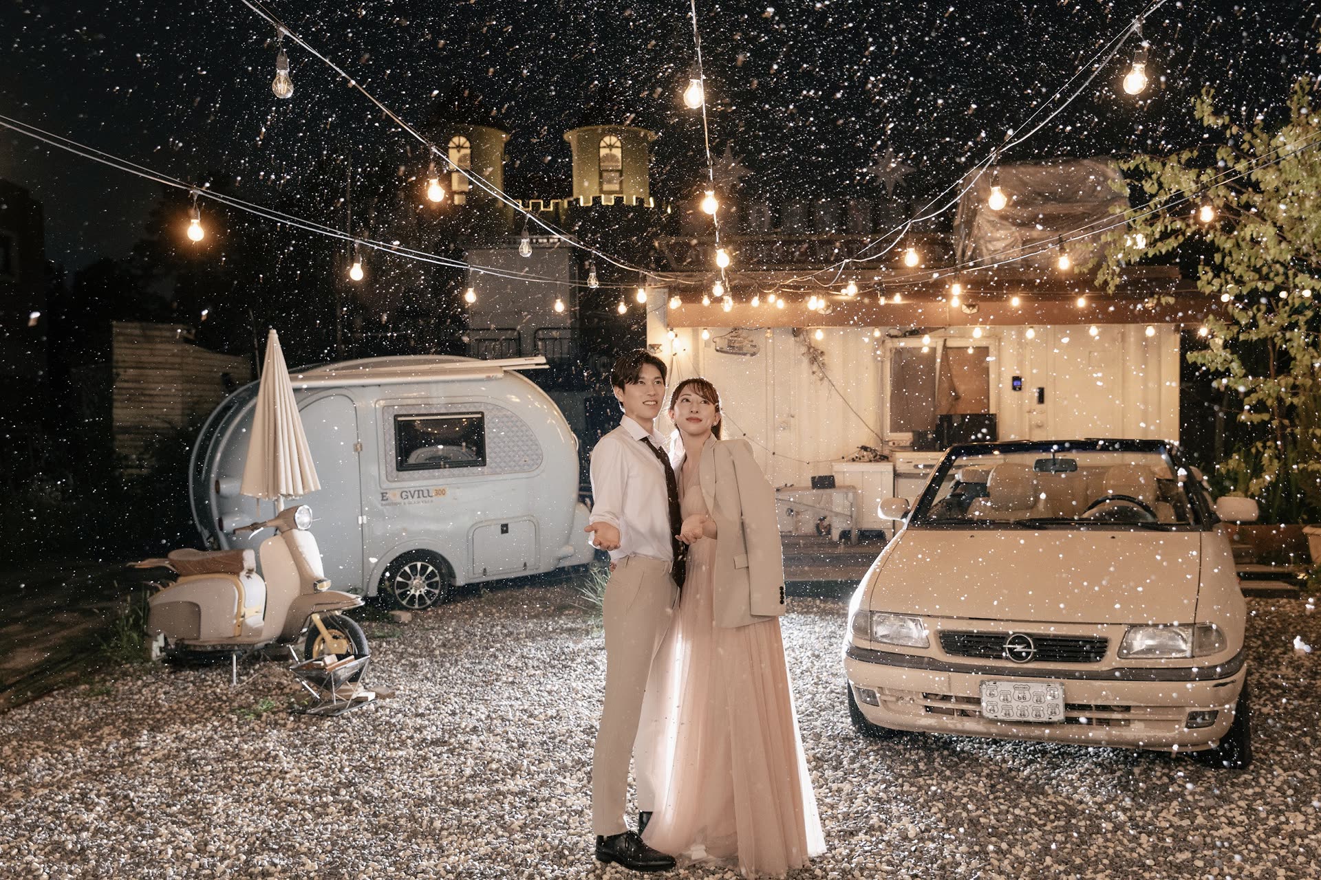 Couple standing under festoon lights as snow falls at a winter photoshoot in Japan