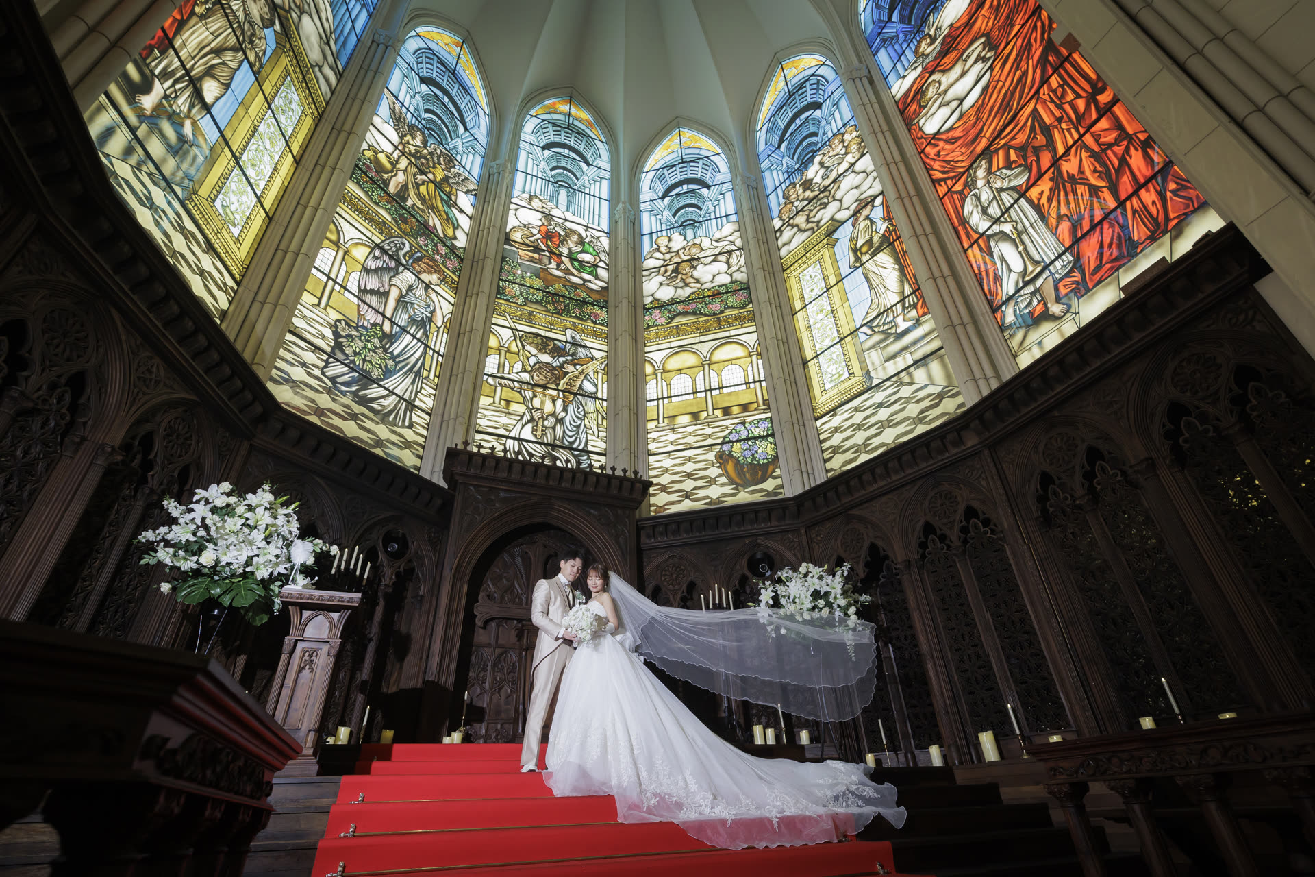 Bride and groom on the chapel steps beneath a vaulted stained-glass window in Japan, photographed by the team behind TAMAKI