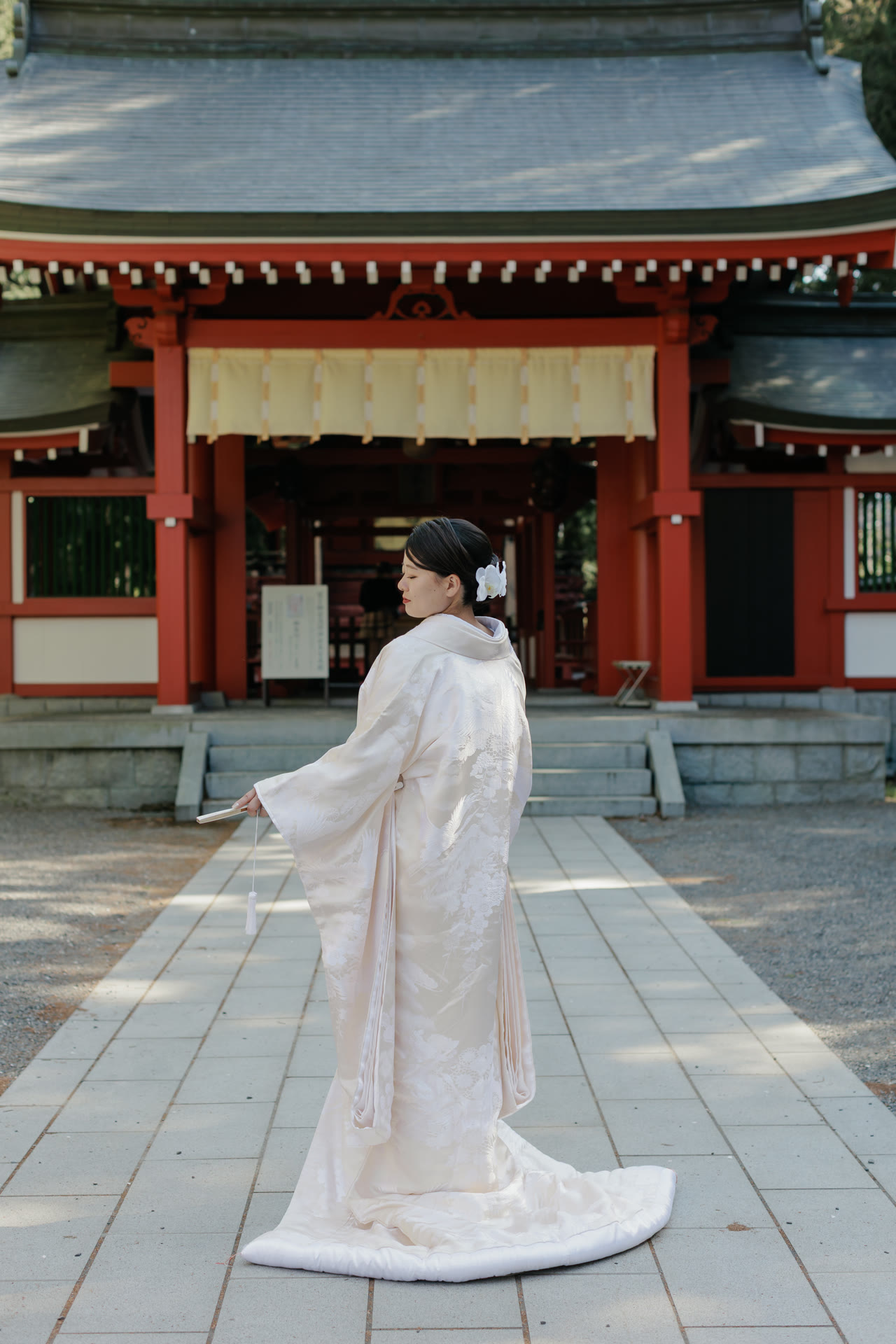 Bride seen from behind spreading the sleeve of her shiromuku before a shrine hall