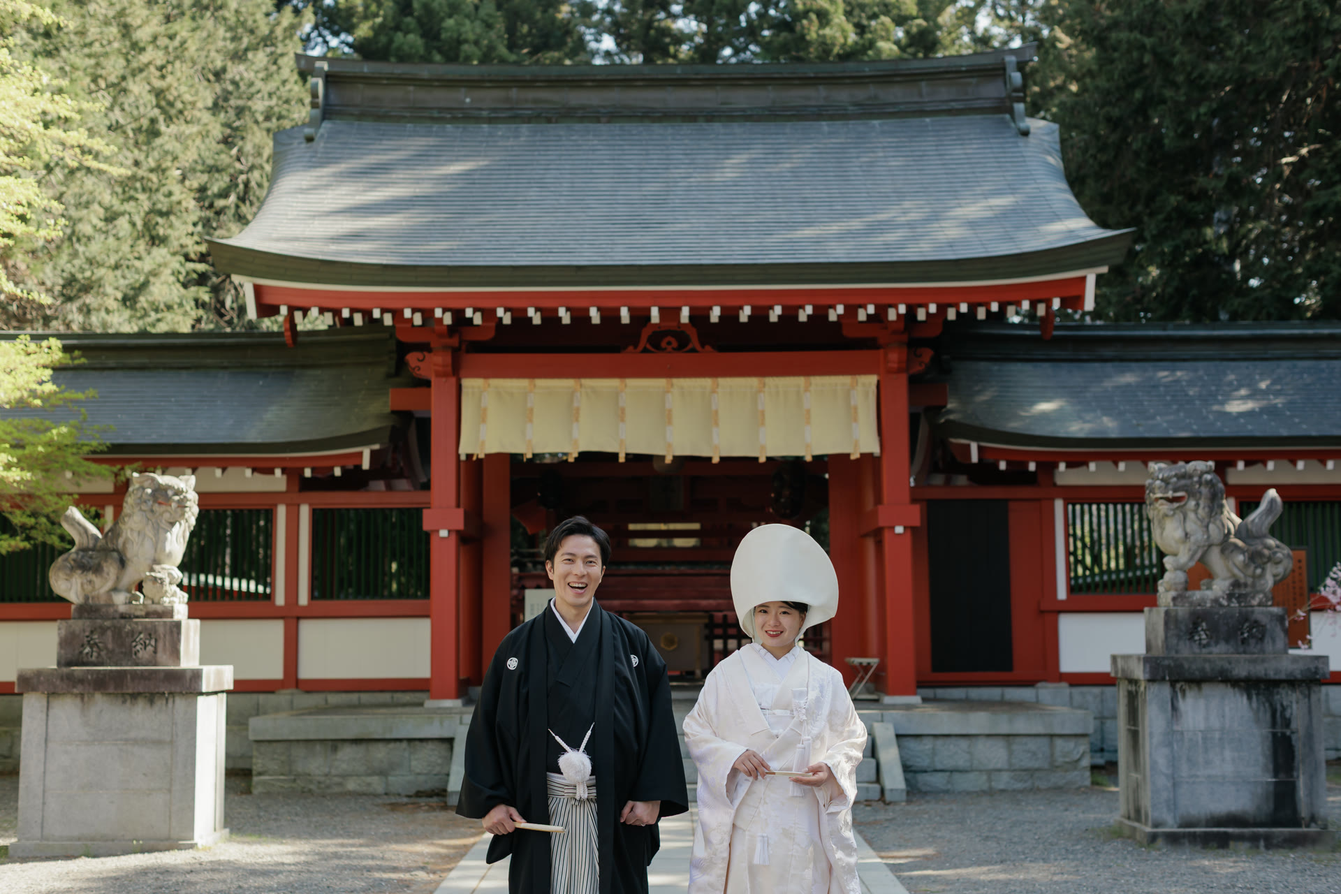 Couple in traditional dress before a shrine hall, flanked by stone komainu guardian lions
