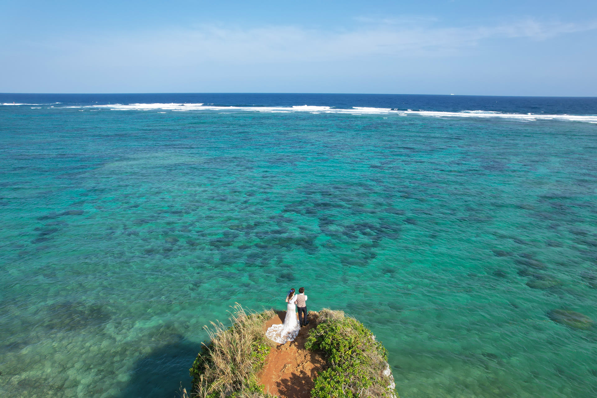 Aerial view of a couple standing on a coral outcrop surrounded by turquoise reef water during an Okinawa pre-wedding photoshoot