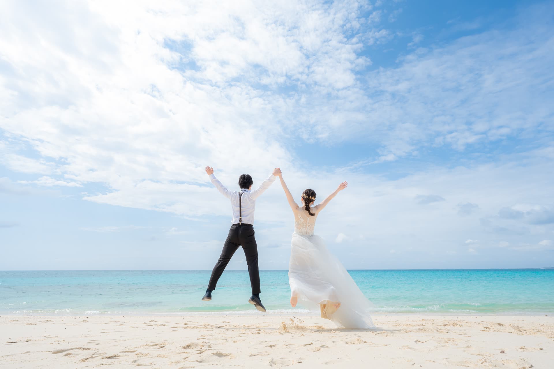 Couple jumping together on an Okinawa beach under a bright blue sky