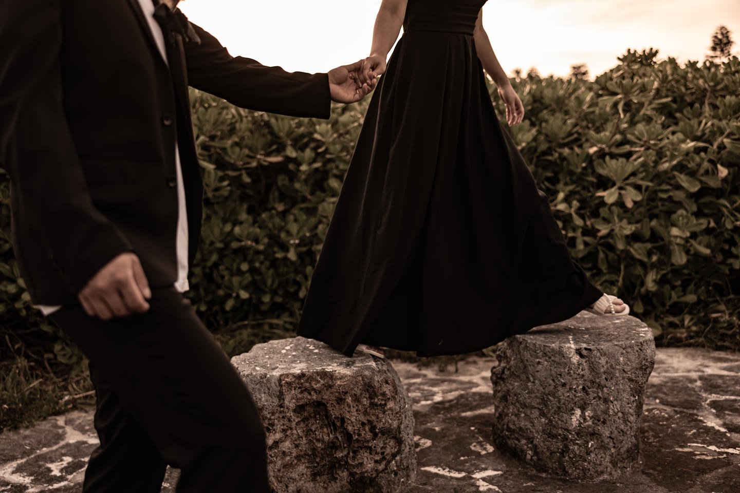 Bride in a black dress on coastal rocks at sunset