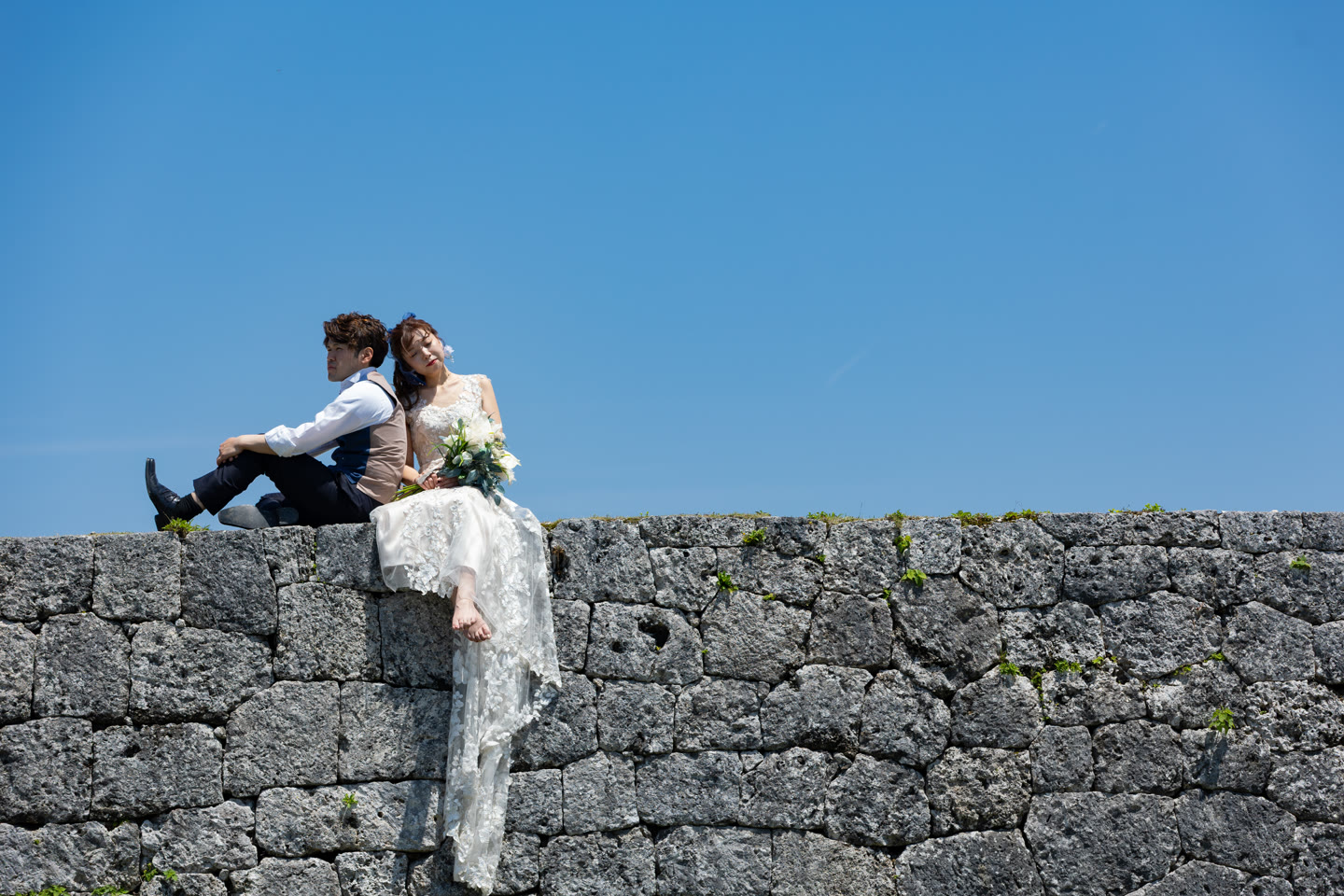 Couple seated on a coral stone wall under a bright blue Okinawa sky