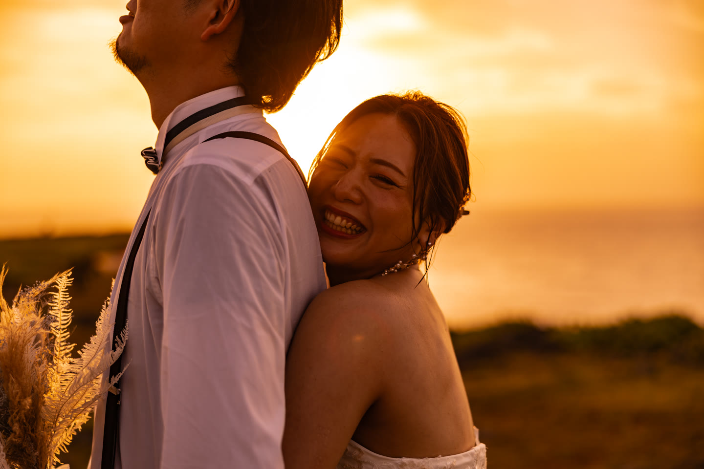 Bride resting against the groom, backlit by the setting Okinawa sun