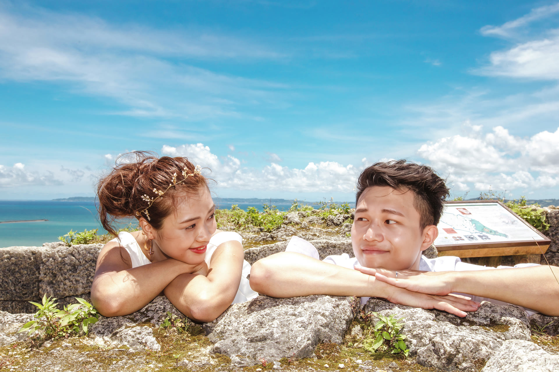 Couple resting on a limestone wall with turquoise Okinawa water behind