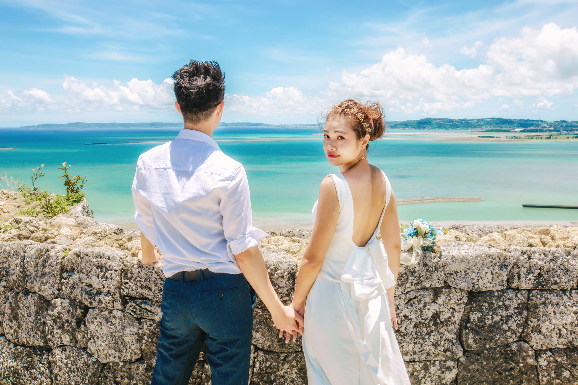 Couple holding hands on a stone wall above the Okinawa sea