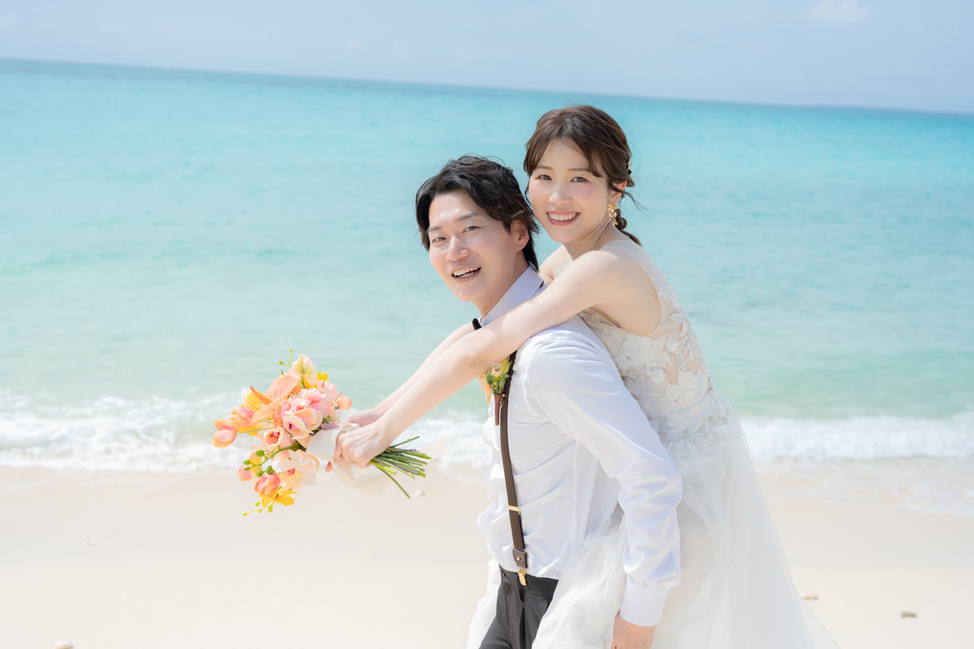 Bride carried piggyback holding a coral bouquet at the Okinawa shoreline
