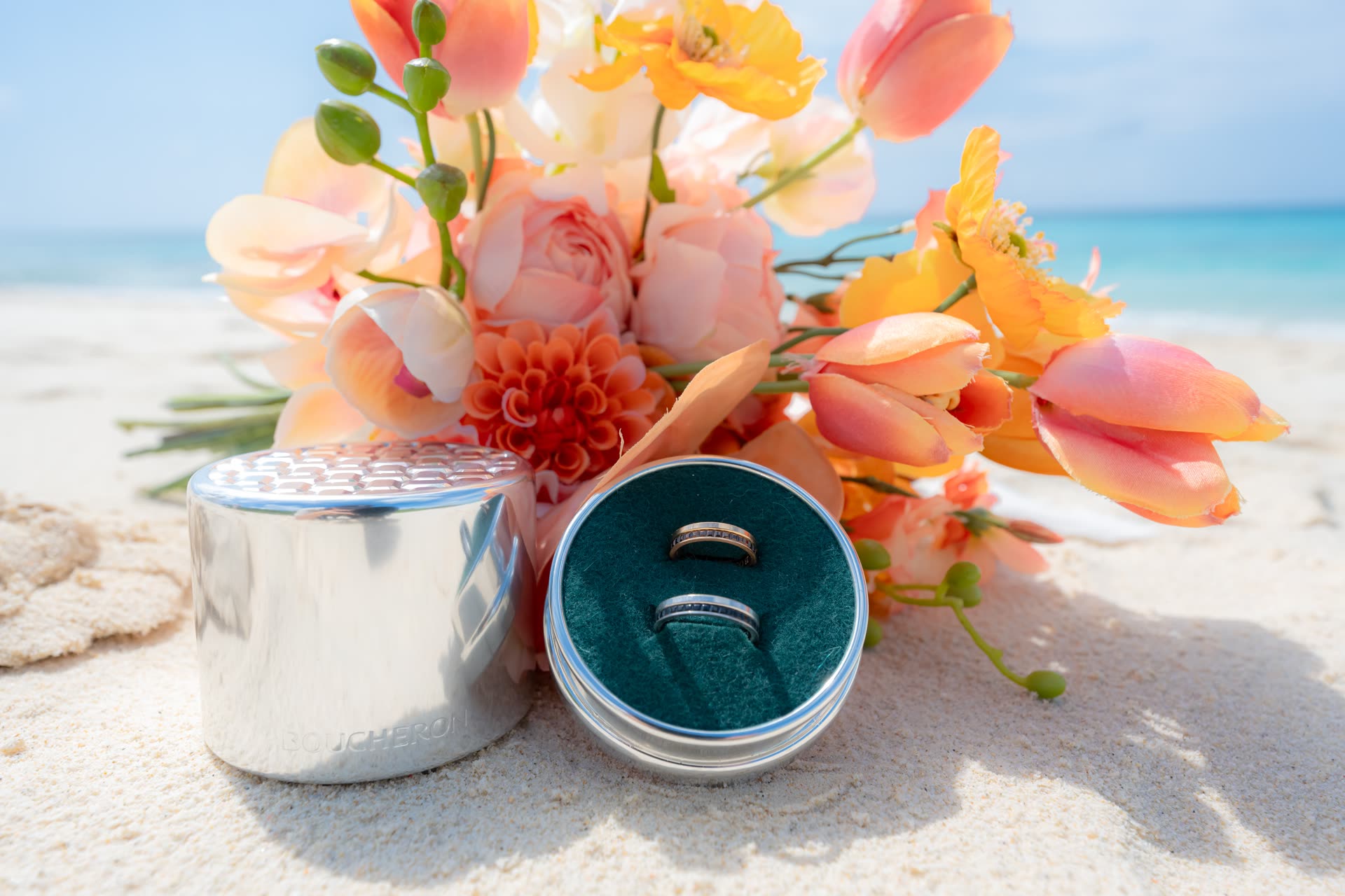 Wedding rings in an open case beside a tropical bouquet on Okinawa white sand