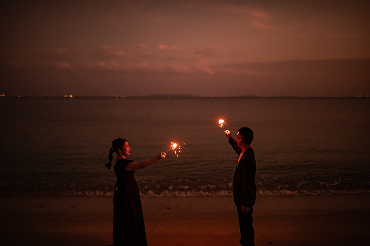 Couple holding sparklers at dusk at the water's edge in Okinawa