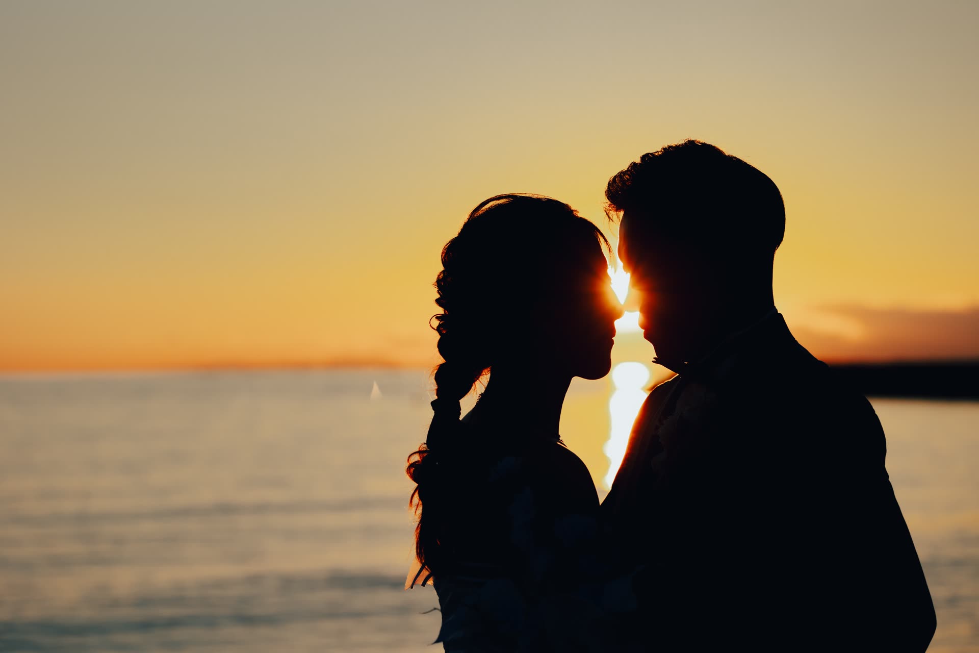 Couple face to face in silhouette as the sun sets over the Okinawa sea