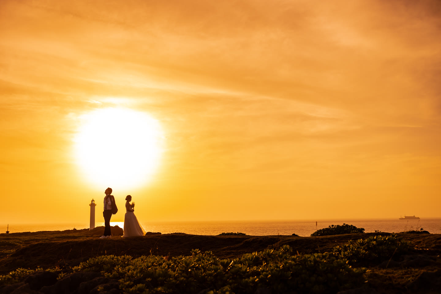 Couple standing small beneath a large setting sun in Okinawa