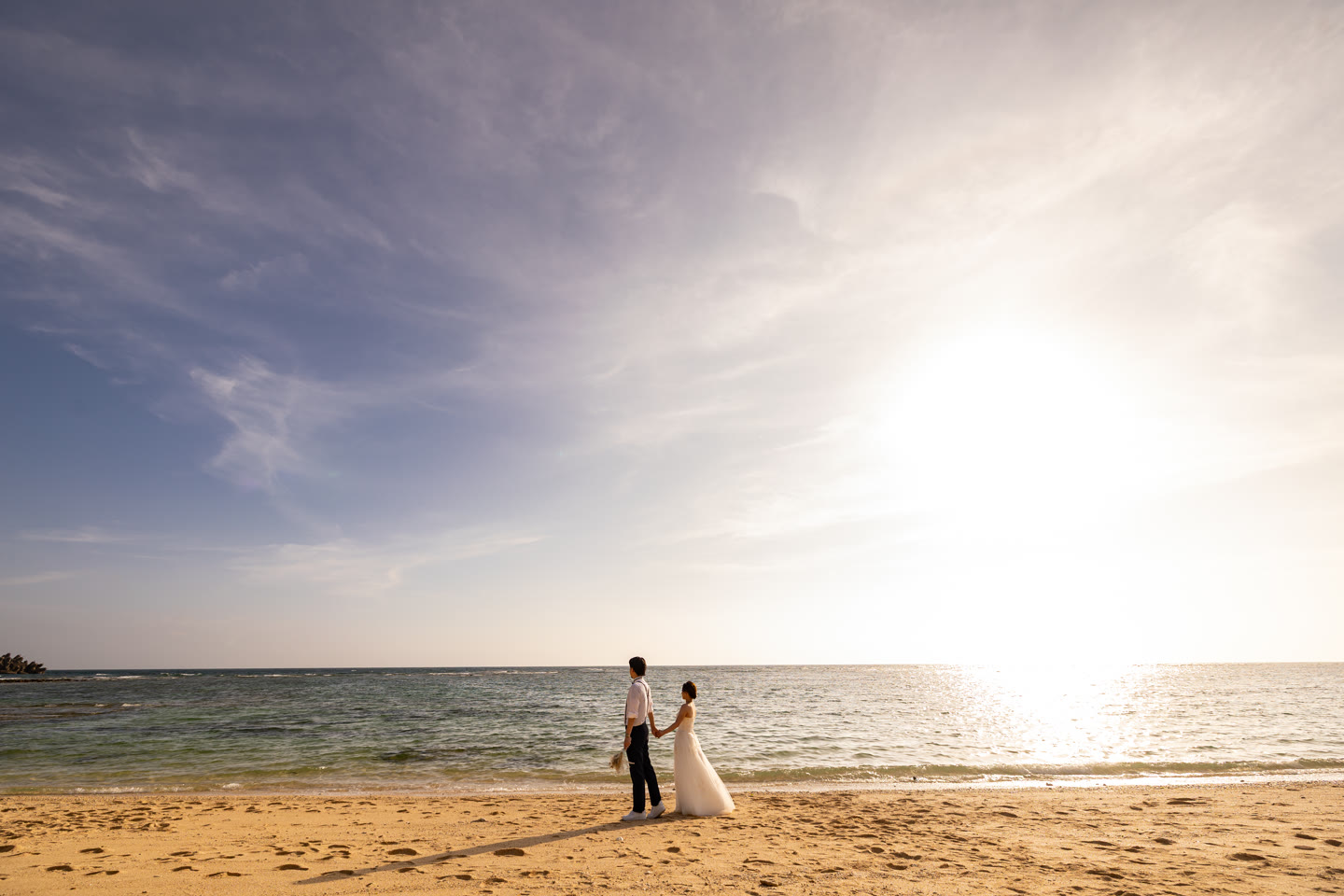 Couple small on the shoreline as the sun meets the Okinawa sea