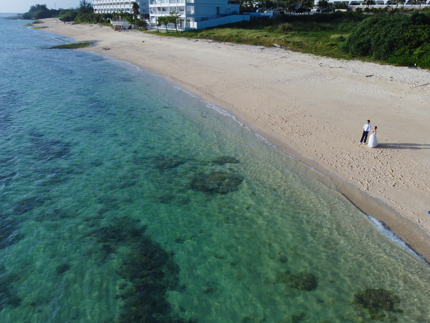 Wide view of a couple on white sand beside turquoise Okinawa water