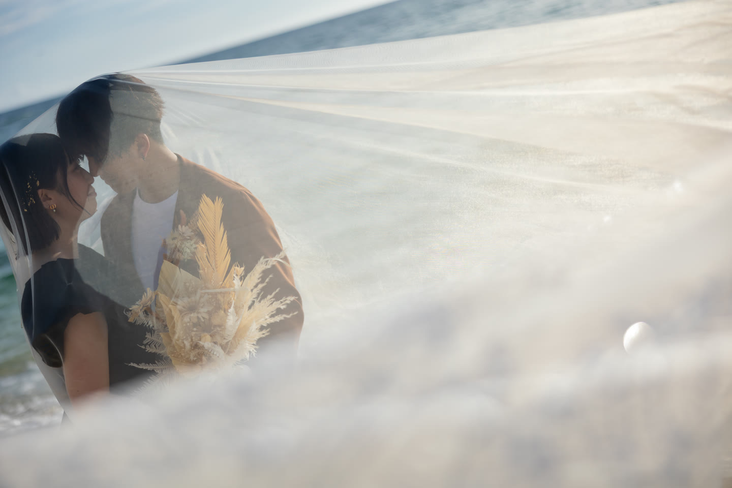 Couple about to kiss beneath a sheer bridal veil