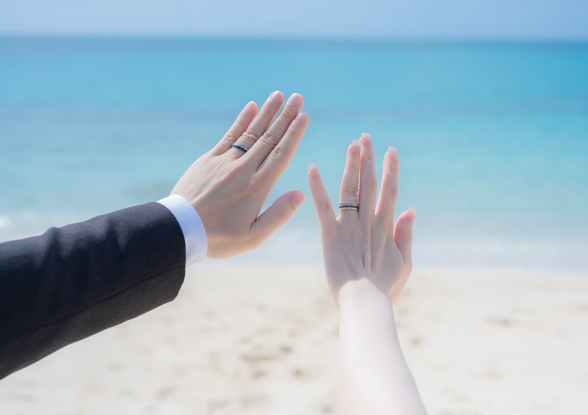 Newlywed hands showing wedding rings against the turquoise water of an Okinawa beach