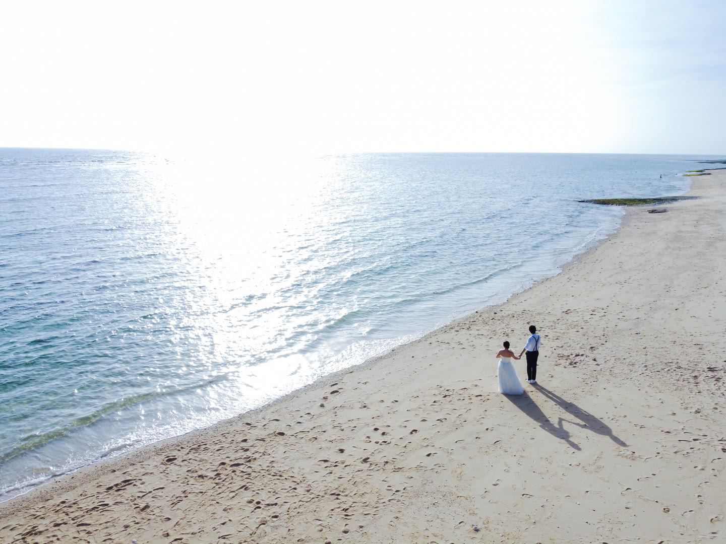 Couple small in the frame on a wide white-sand Okinawa beach