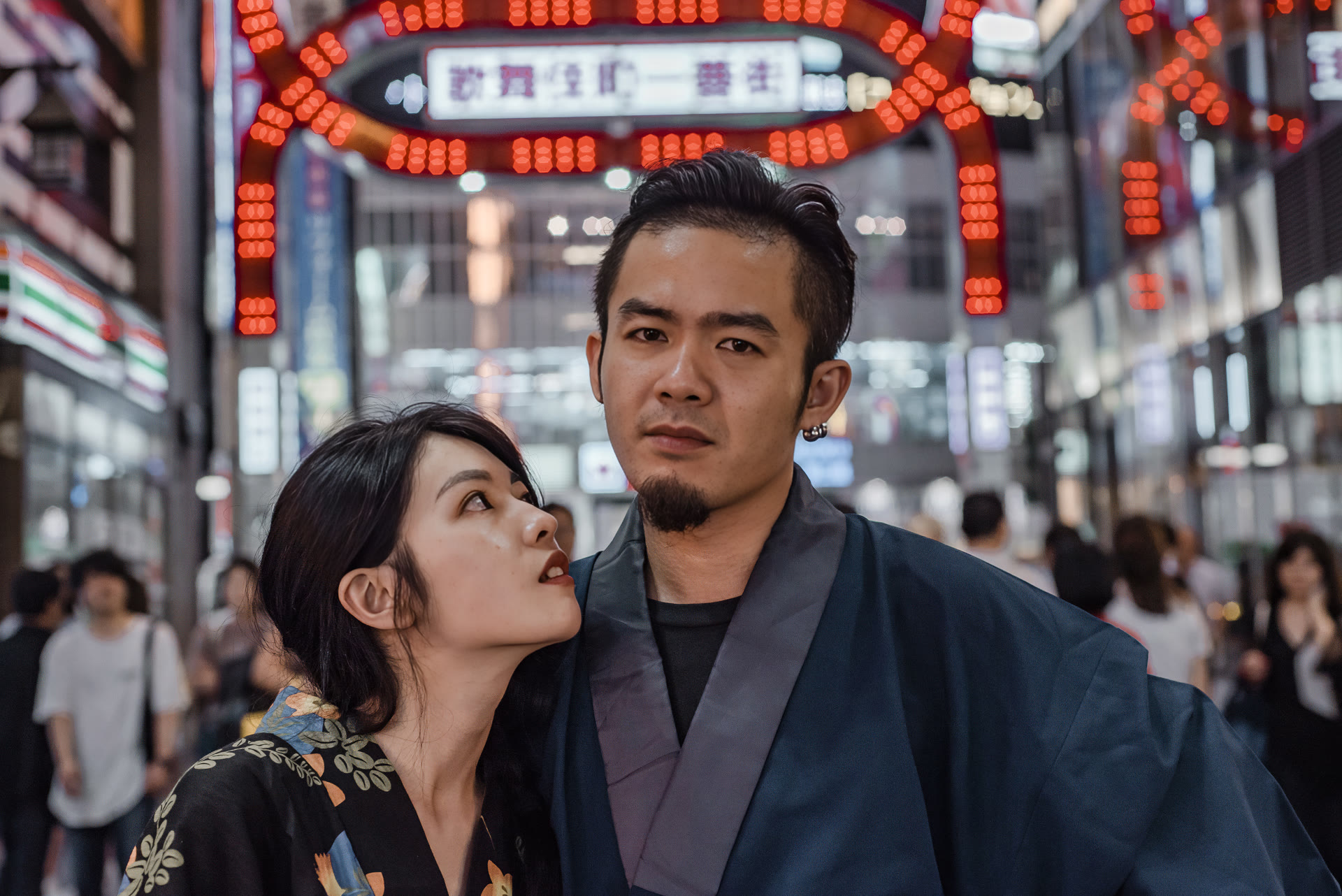 Couple in kimono beneath the neon signs of a Tokyo entertainment district at night