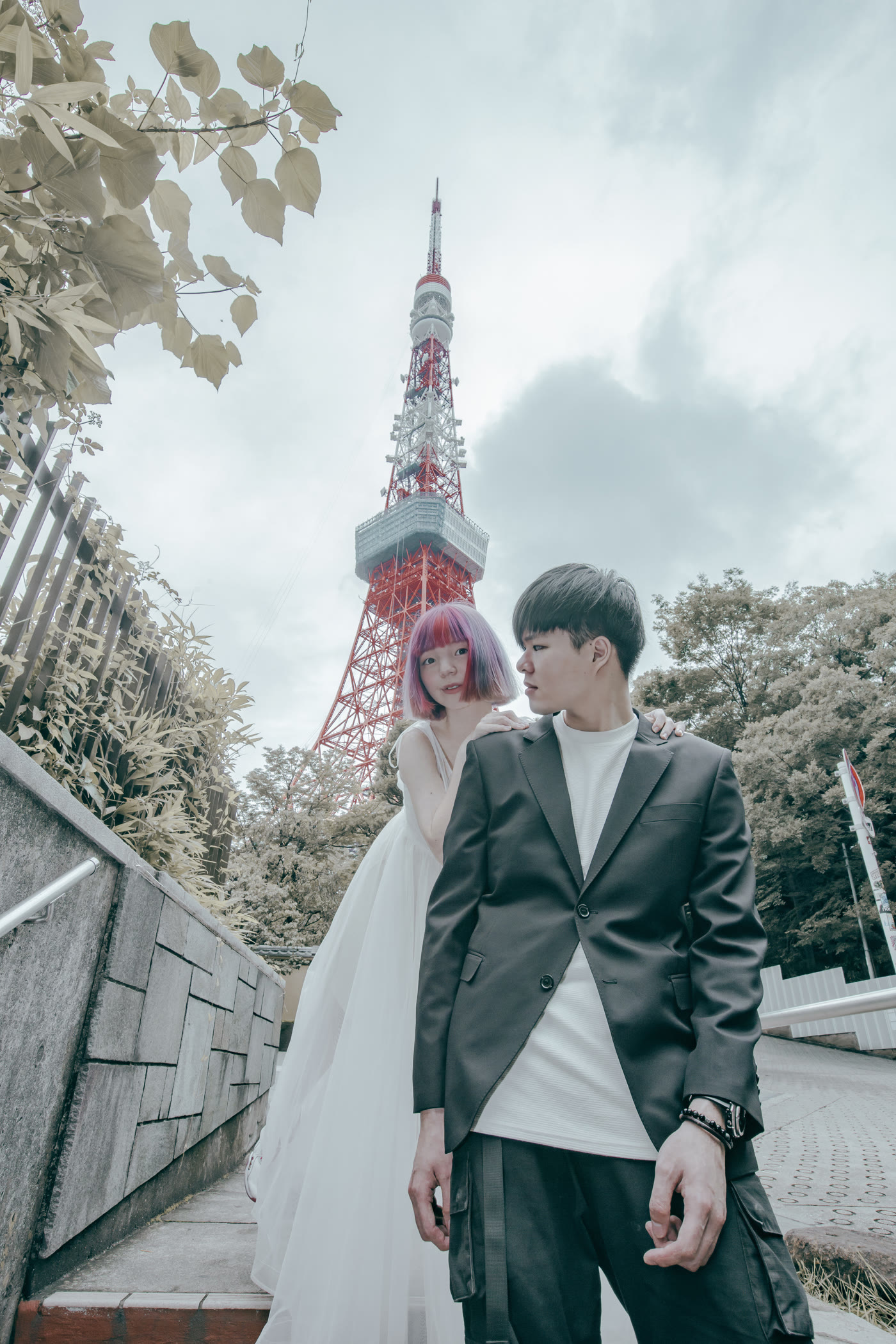 Bride in a tulle gown and groom in a tailored jacket below Tokyo Tower